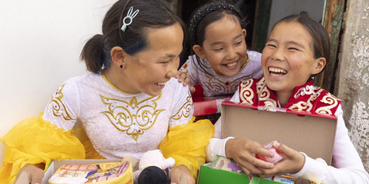 Three smiling young girls exploring their Operation Christmas Child shoebox gifts